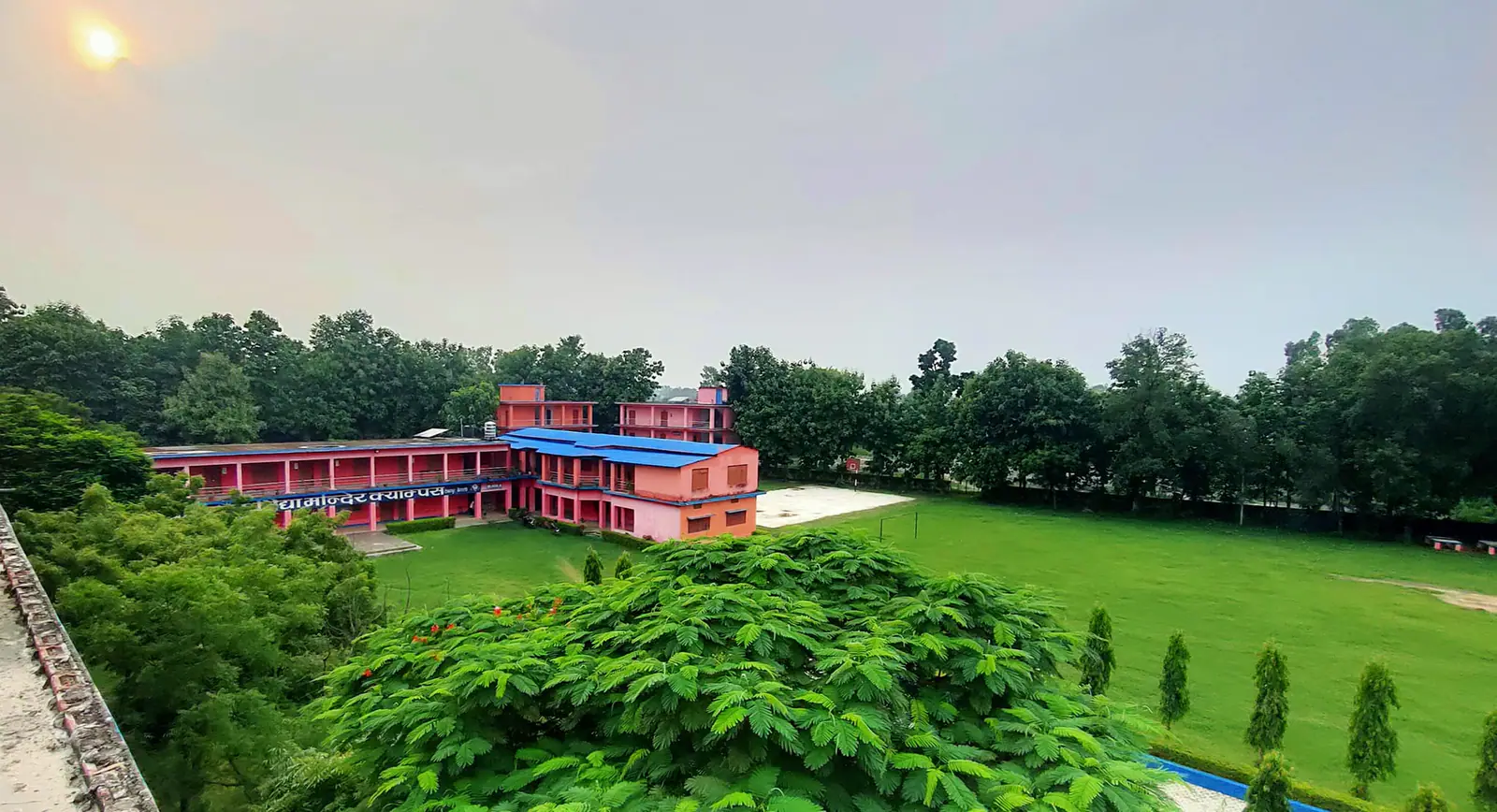 The pink and blue two-storey campus block seen across a wide lawn edged with trees