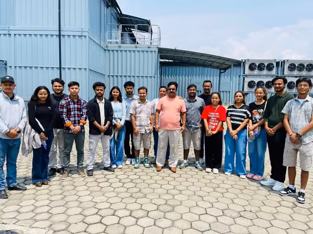 Students outside a steel-clad plant building on a visit, its cooling units ranged along the wall