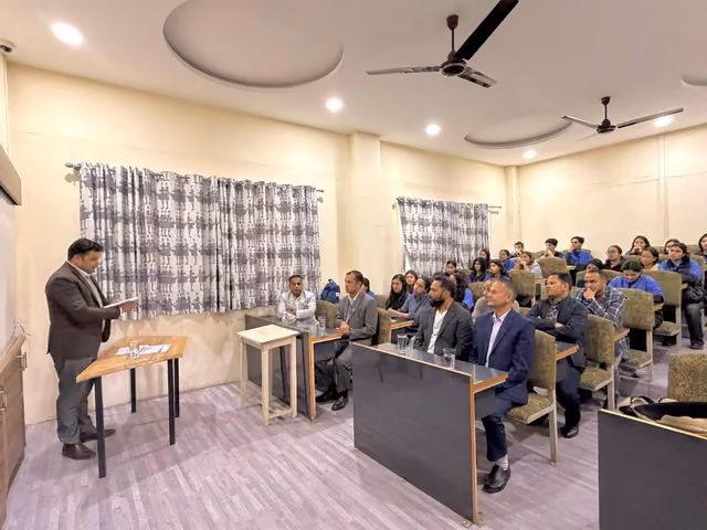A speaker at a lectern addressing students seated at desks in a curtained seminar room