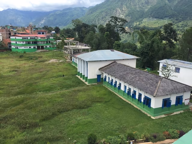 Tin-roofed classroom wings on a green hillside terrace with a taller block behind them