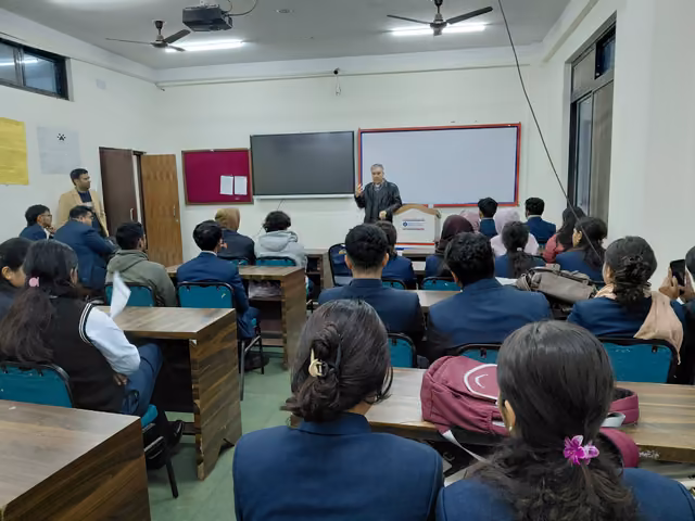 Students in blazers at bench desks facing a speaker beside the whiteboard and screen