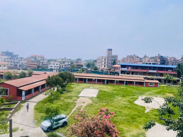 A long red-roofed block across the campus lawn, the rooftops of Lalitpur beyond