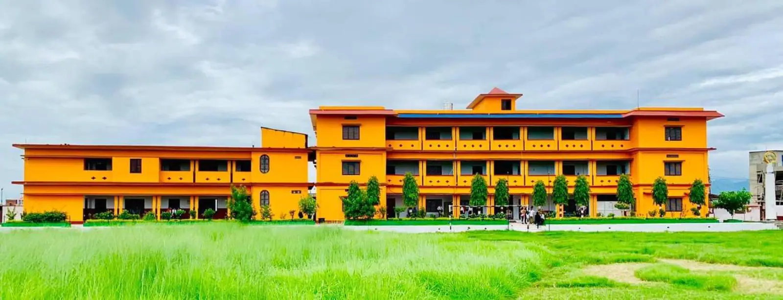 The orange three-storey campus block behind its lawn, hedges clipped along the front