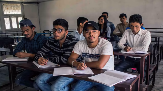 Students writing at shared wooden benches in a plain classroom