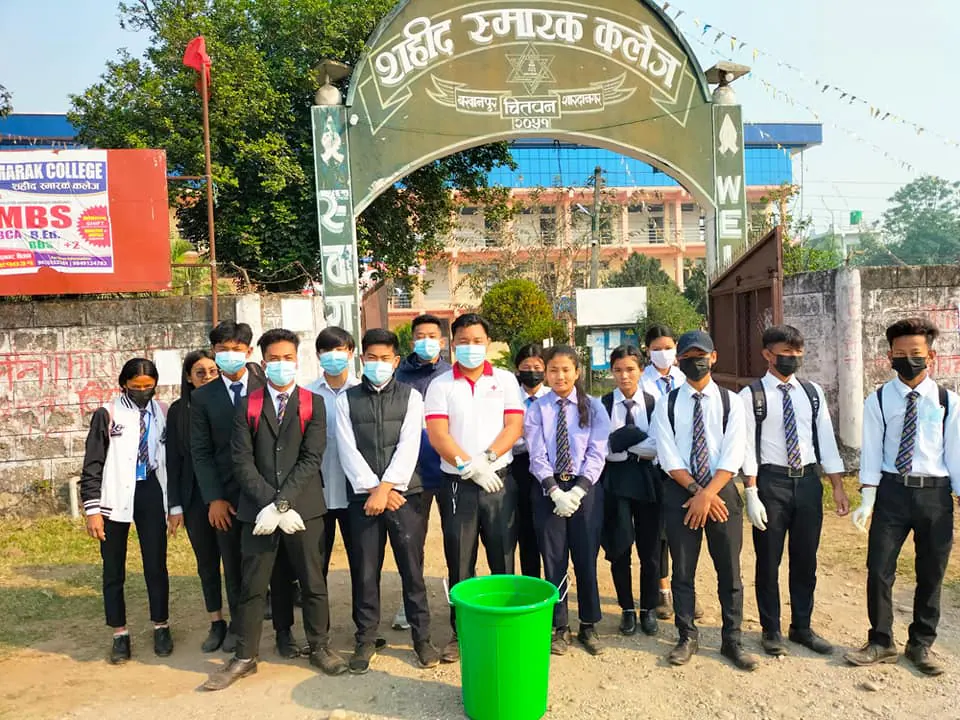 Students lined up at the campus gate, its green arch lettered शहिद स्मारक कलेज
